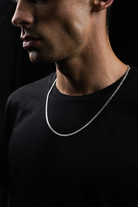 Man wearing a silver chain necklace against a black background