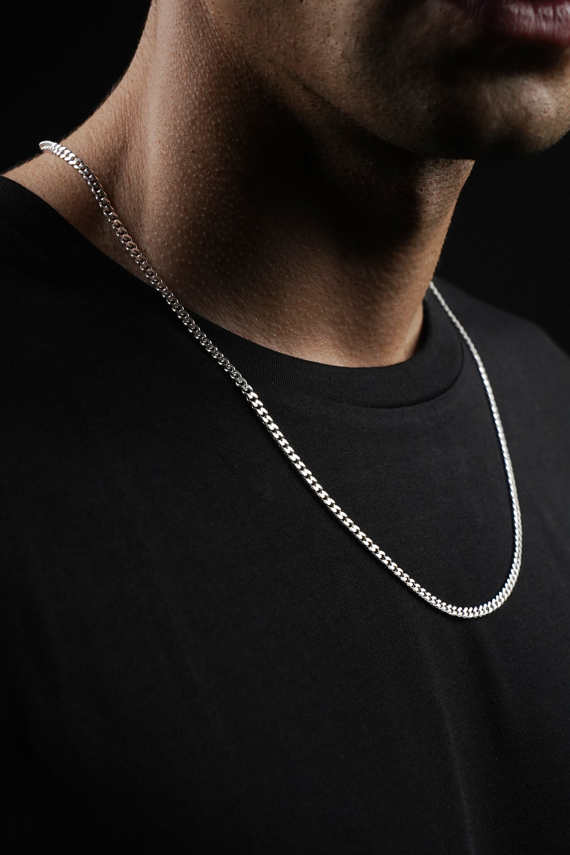Silver chain necklace on a person wearing a black shirt against a dark background