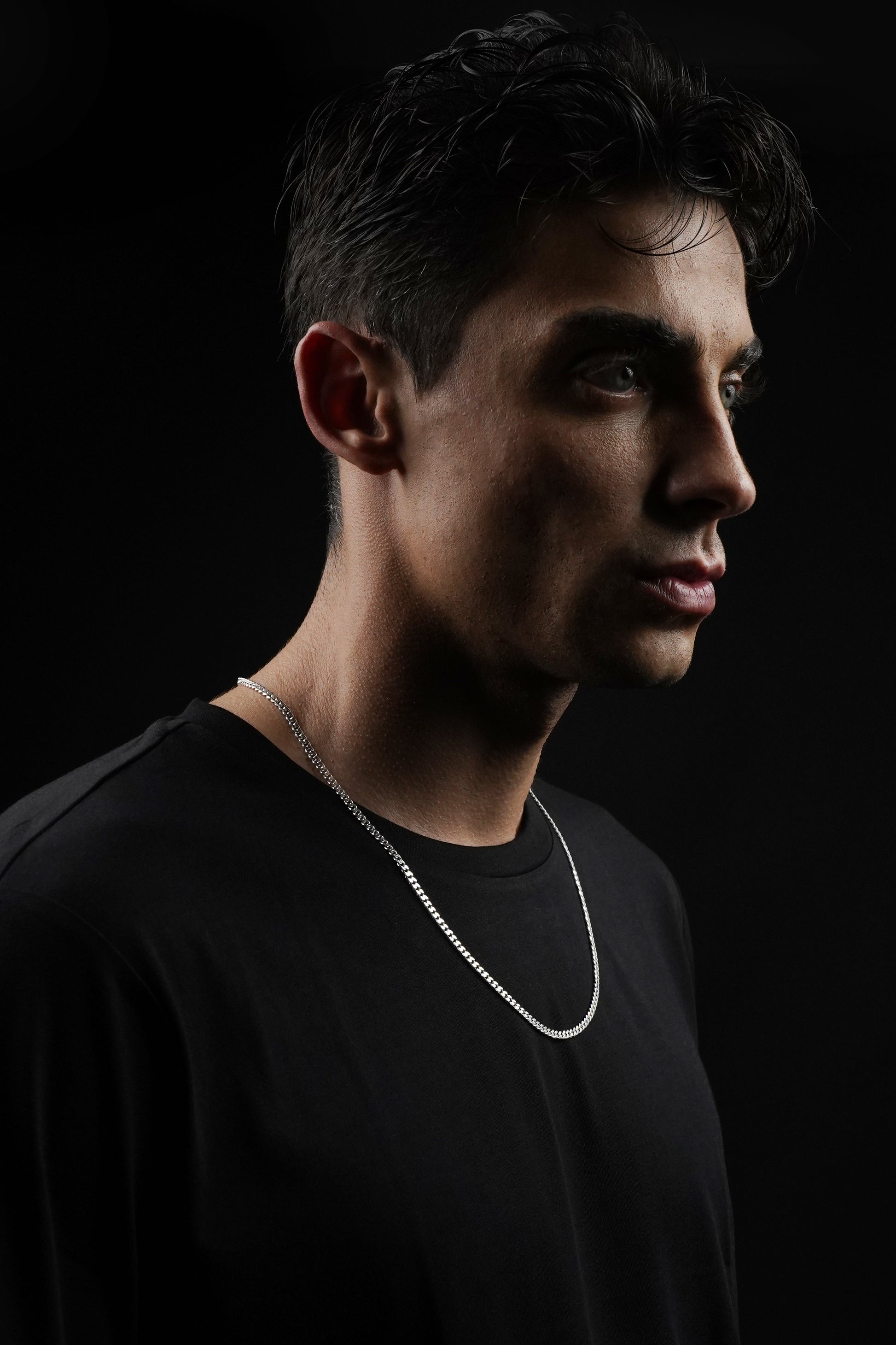 Man wearing a black shirt and silver necklace against a dark background